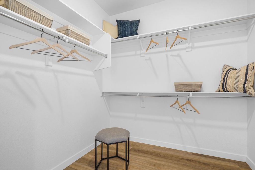 Walk-in closet with white walls, wood floor, and multiple shelves and hanging rods.