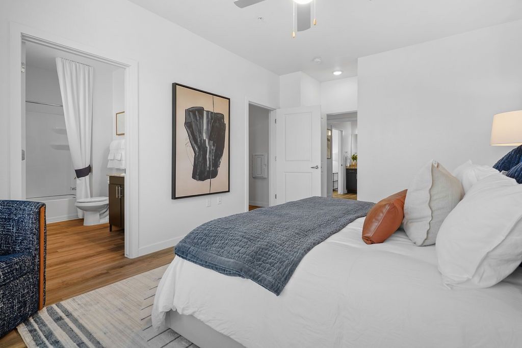 Bedroom in an apartment with a large bed, throw blanket, pillows, and doorway to a bathroom.