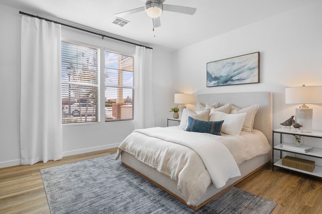 Bright bedroom in a modern apartment with a king bed, white bedding, two nightstands, and a large window with blinds.
