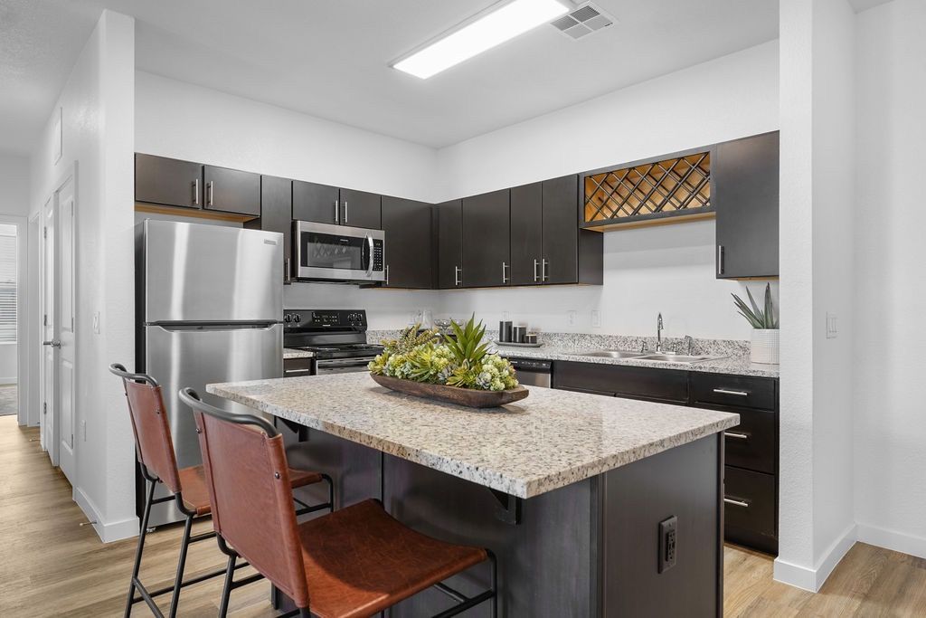 Modern kitchen with granite island, dark cabinets, and stainless-steel appliances.