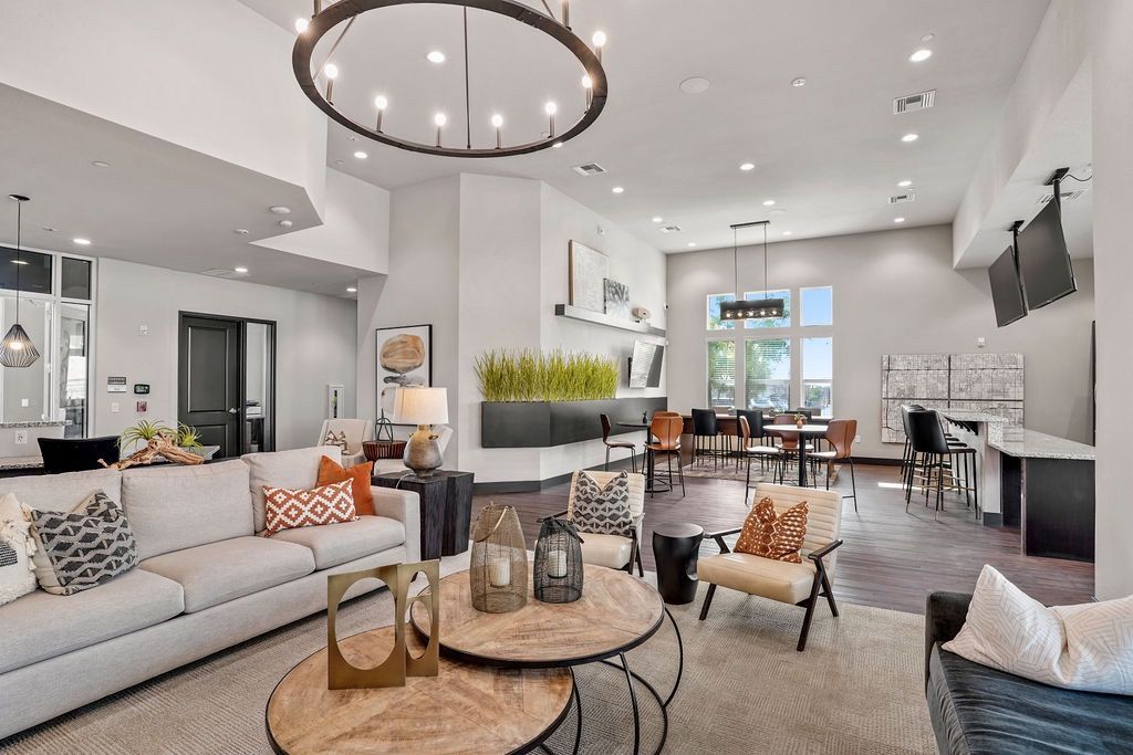 Bright, modern community lounge with sofa seating, chairs, and a kitchenette.