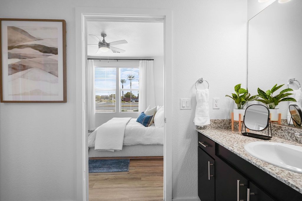 Bathroom vanity with granite countertop and mirror, opening to a bright bedroom.
