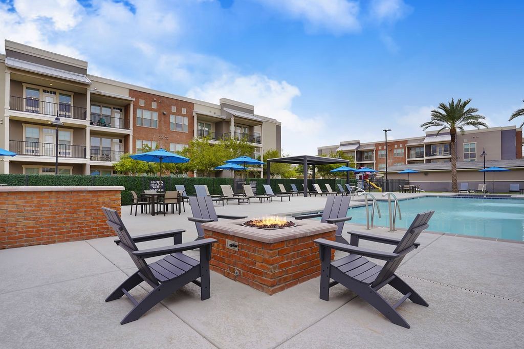 Outdoor pool area with lounge chairs, blue umbrellas, and a central fire pit.