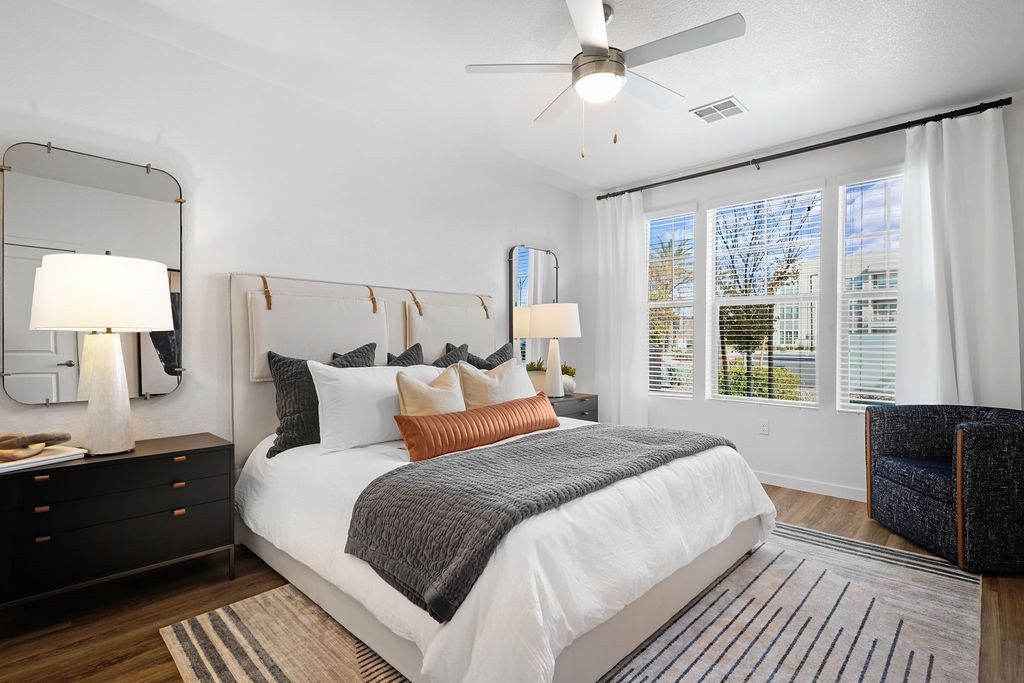 Bedroom with a king-size bed, two nightstands, lamps, ceiling fan, and a large window with white curtains.