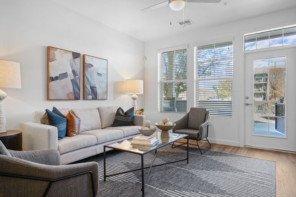 Bright living room with white sofa, two chairs, glass coffee table, and large windows.
