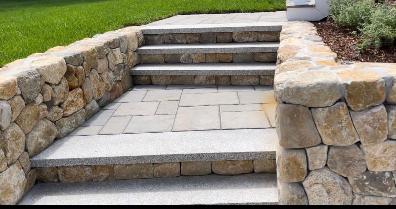 Stone stairs with granite treads flanked by matching stone retaining walls in a garden setting.