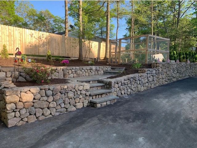 A multi-level stone retaining wall with integrated steps leading to a raised garden area and a wooden outdoor enclosure.