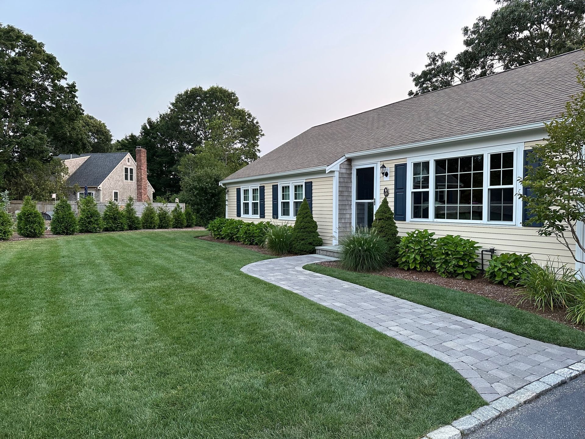 A yellow house with dark shutters, a stone walkway, and a neatly mowed green lawn under a clear sky.