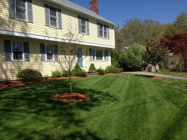 Yellow two-story house with a chimney and neatly mown lawn under a clear blue sky.