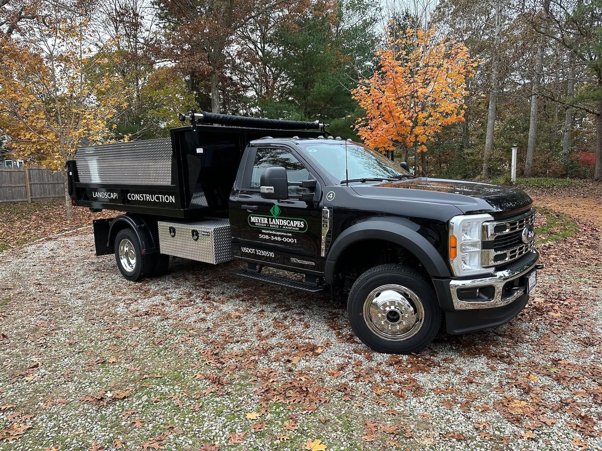 A black Ford dump truck parked on a gravel driveway surrounded by trees with autumn leaves.