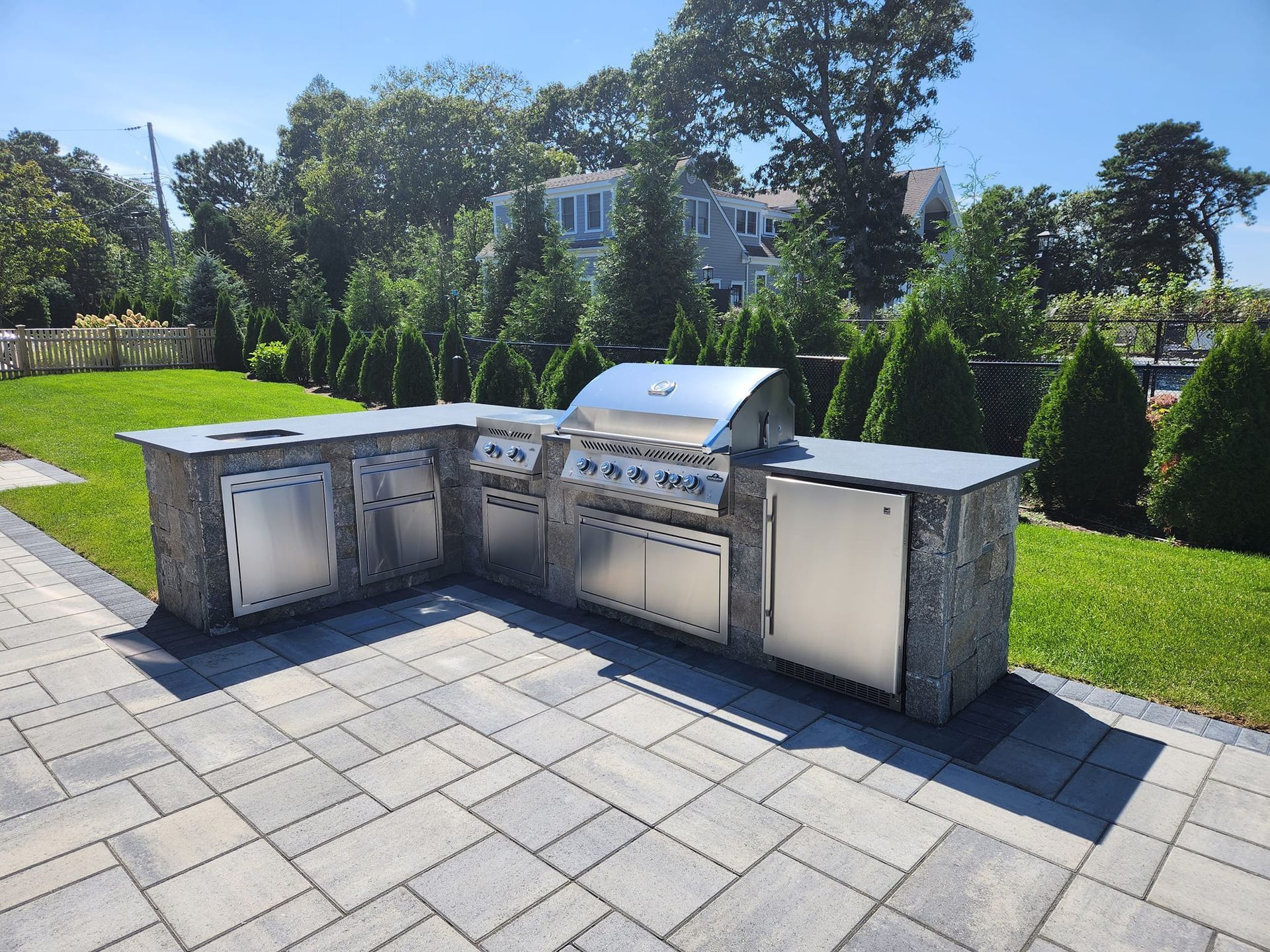 A stainless steel grill is sitting on a patio in a backyard.