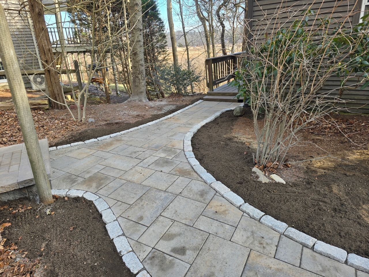 A brick walkway leading to a house in the woods.