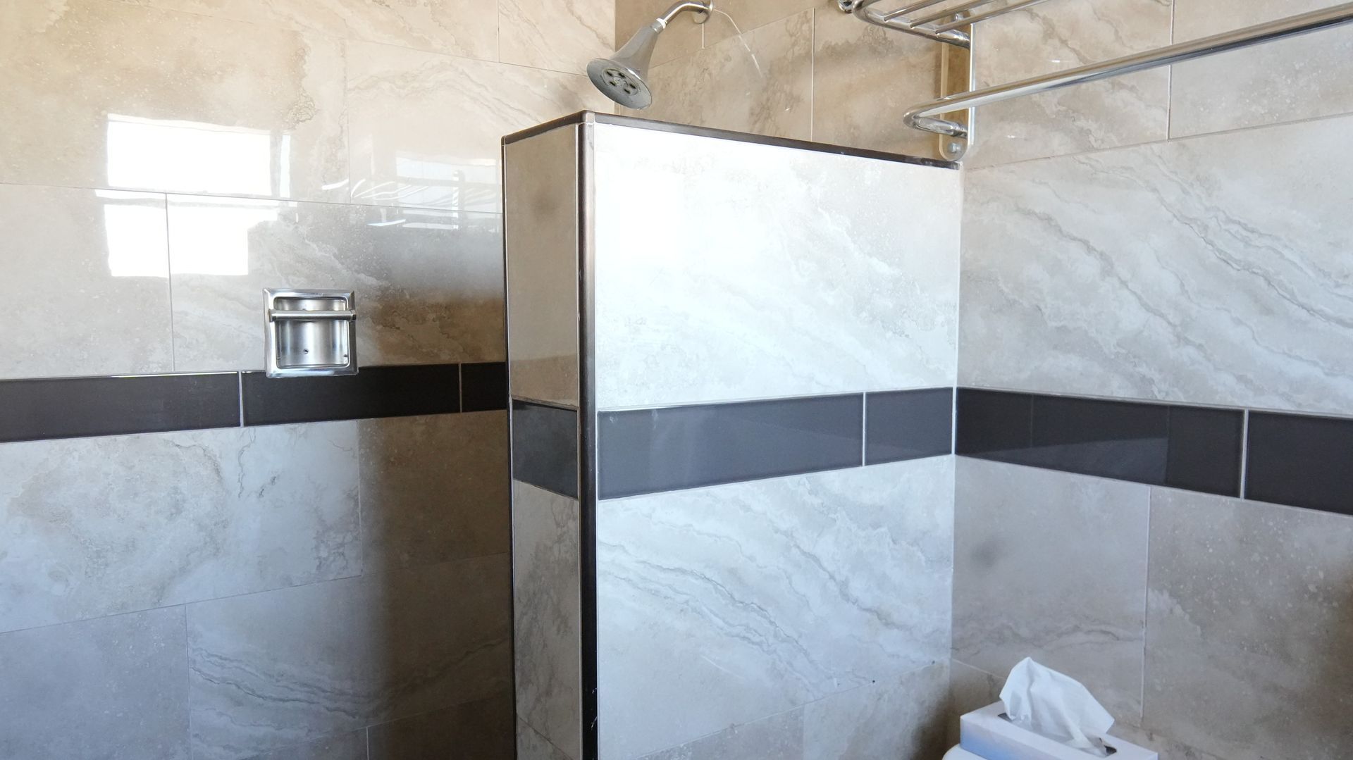 Bathroom with light gray tiled walls, shower with chrome fixtures, and a dark gray accent band.