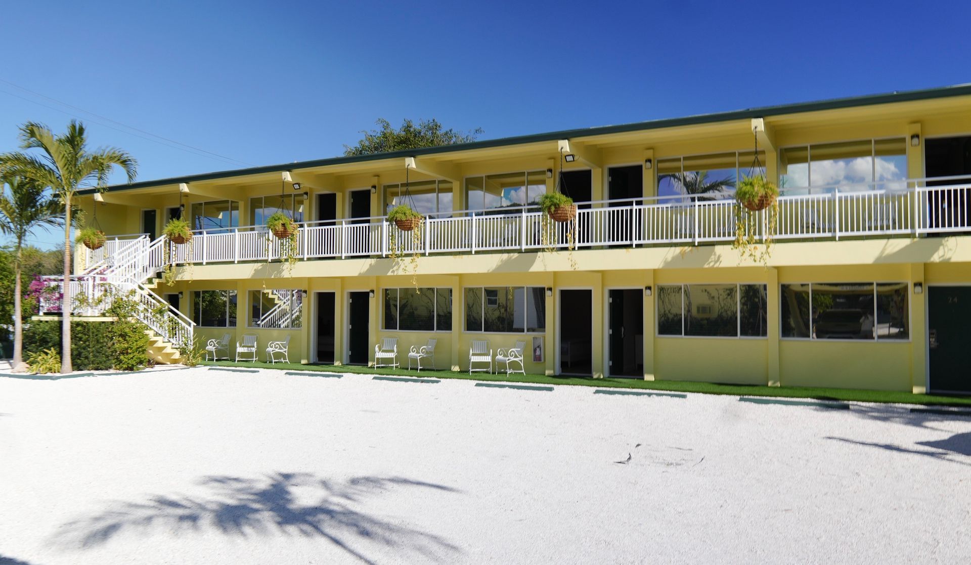 Two-story motel with yellow walls, white railings, and hanging flower baskets under a blue sky.