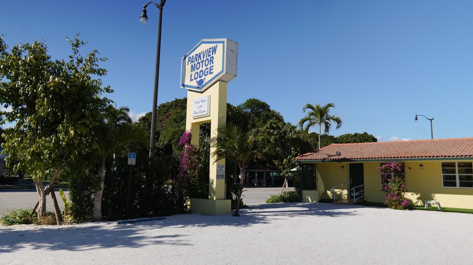 Sign for Angler's Motel & Lodge; cream-colored, with a yellow building and light blue sky.