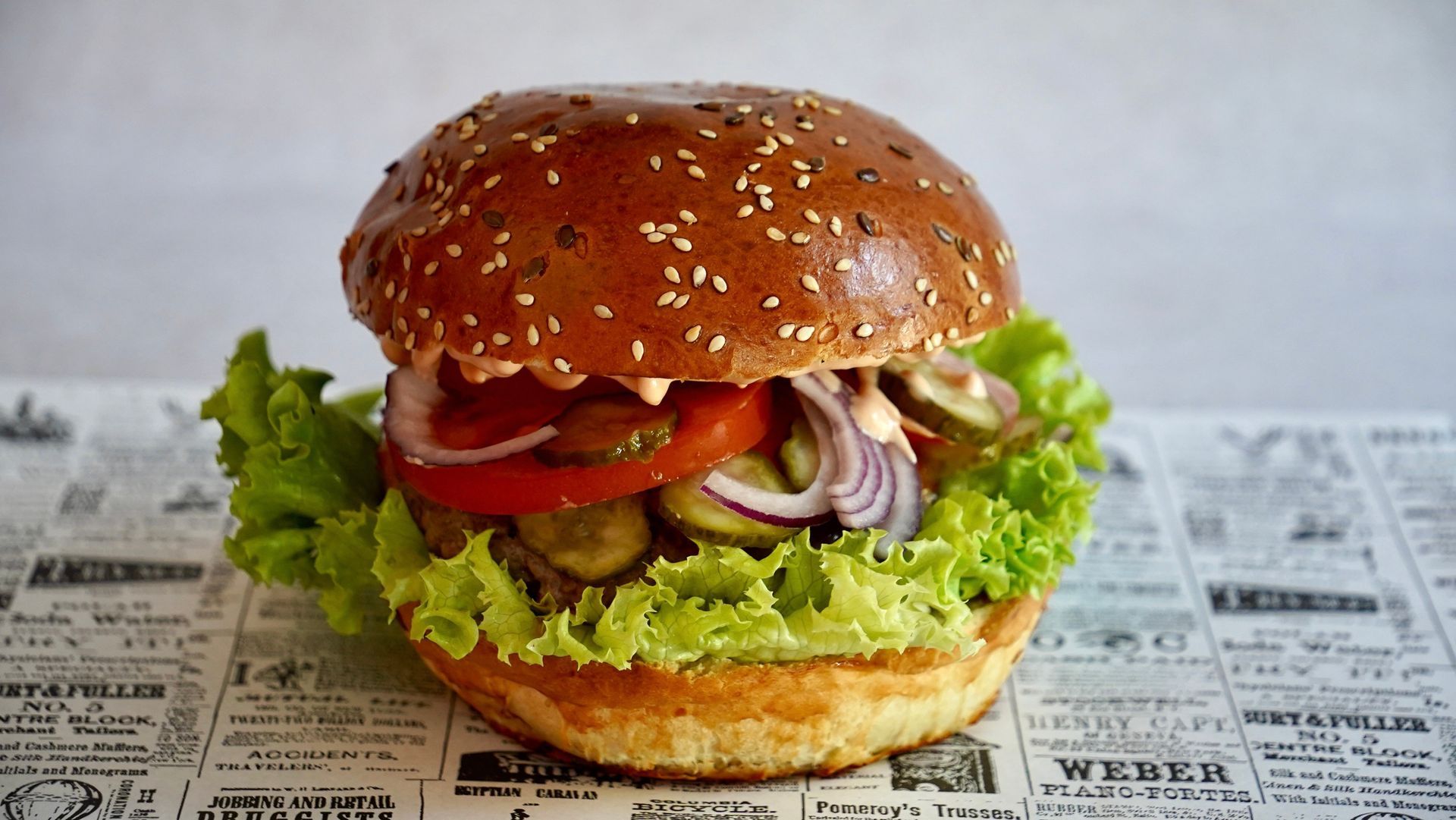 Burger on a bun with lettuce, tomato, pickles, and onion on a patterned surface.