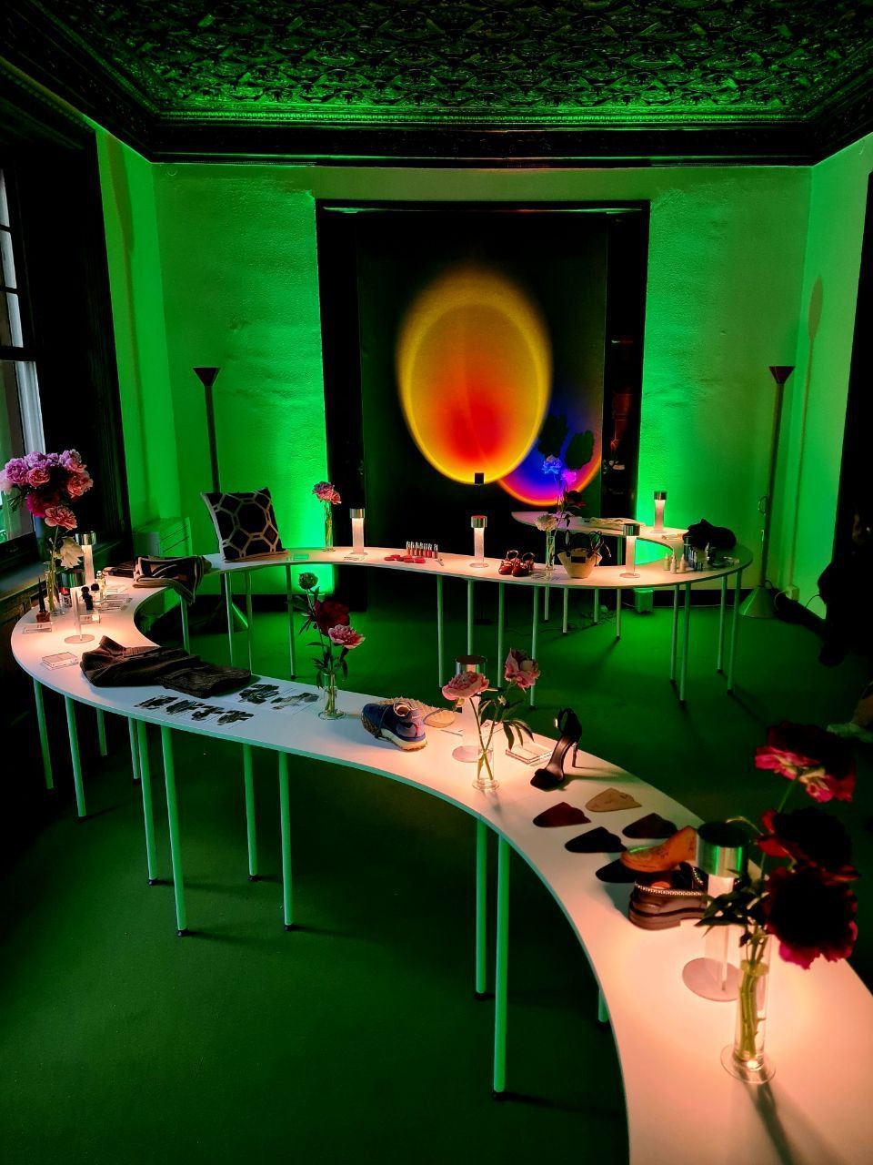 Una stanza con un lungo tavolo bianco e curvo su cui sono esposti oggetti; illuminata da una luce verde, con opere d'arte alle pareti.