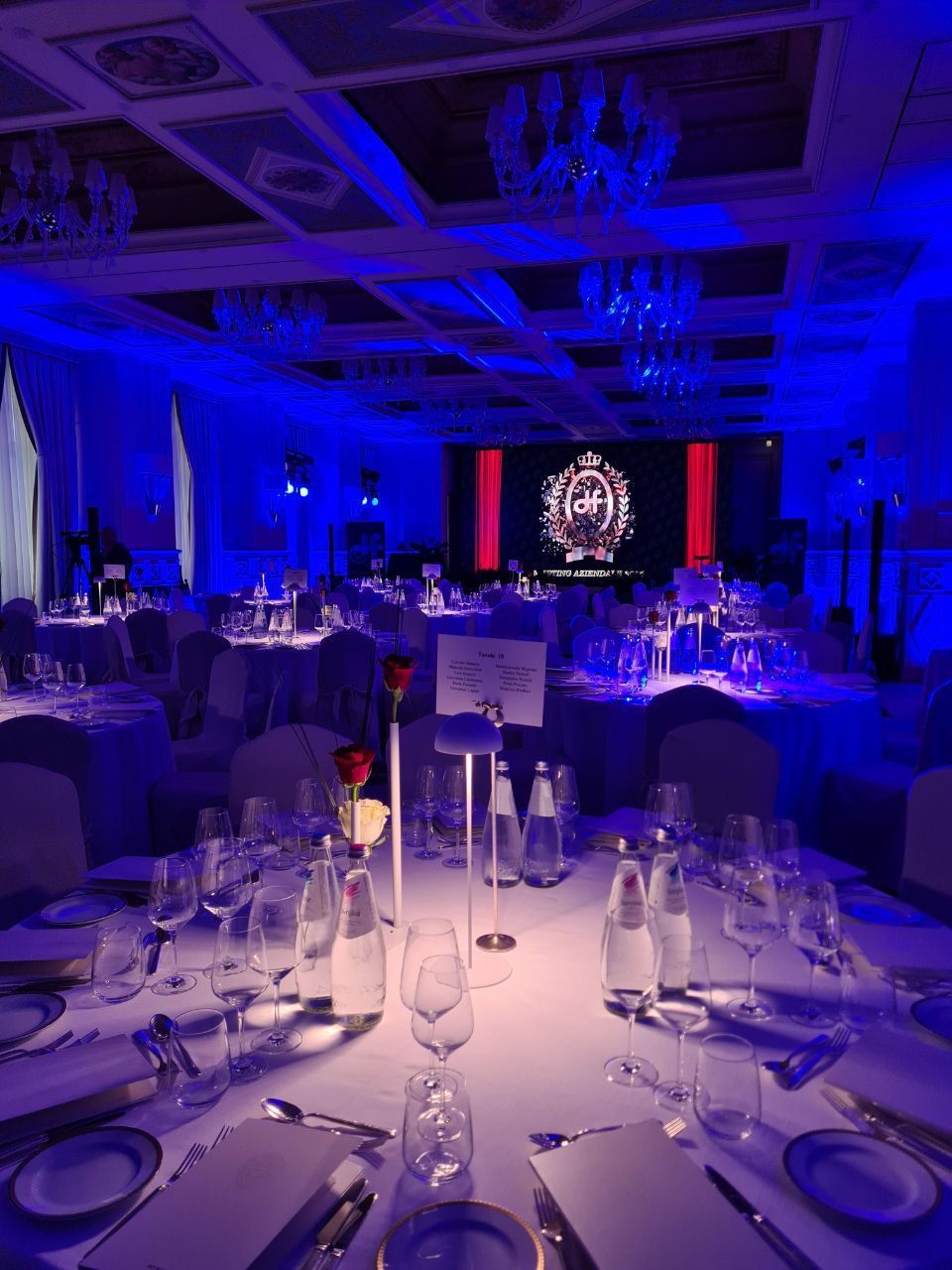 Cena formale con tavoli, apparecchiati e una composizione floreale centrale immersa nella luce blu.