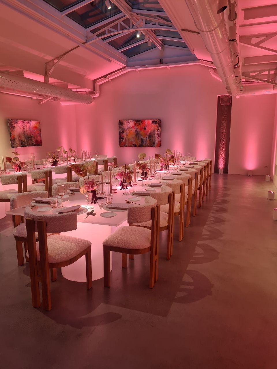 Lunghi tavoli da pranzo apparecchiati per un pasto in una stanza illuminata di rosa.