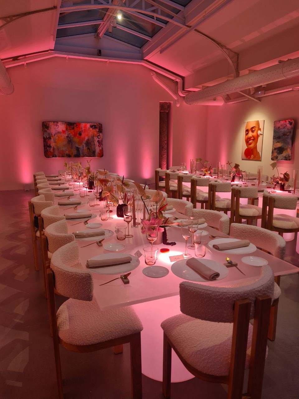 Elegante sala da pranzo con illuminazione ambientale rosa e lunghi tavoli apparecchiati per il pasto.
