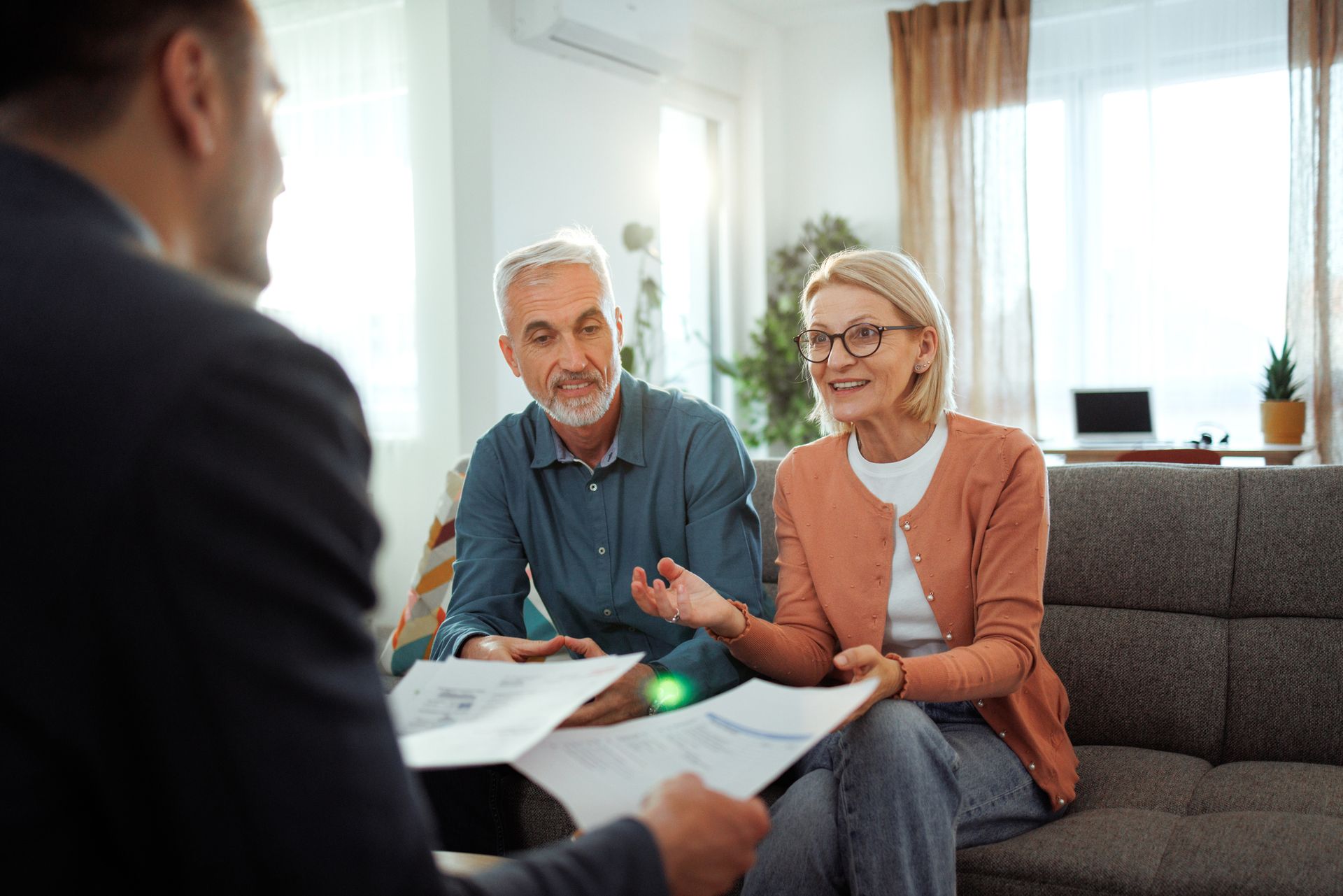 Financial advisor presenting documents to an older couple on a couch in a living room.