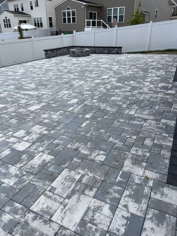 Large paved patio with a fire pit, enclosed by a white fence, gray and white pavers.