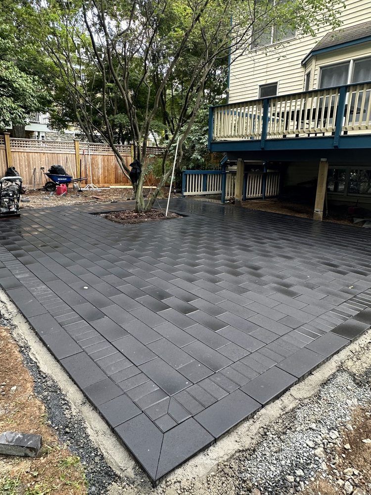 Newly paved patio with black rectangular pavers, adjacent to a wooden deck and backyard.