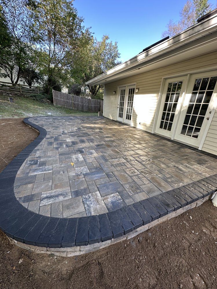 Brick patio with a curved border beside a beige house with French doors.