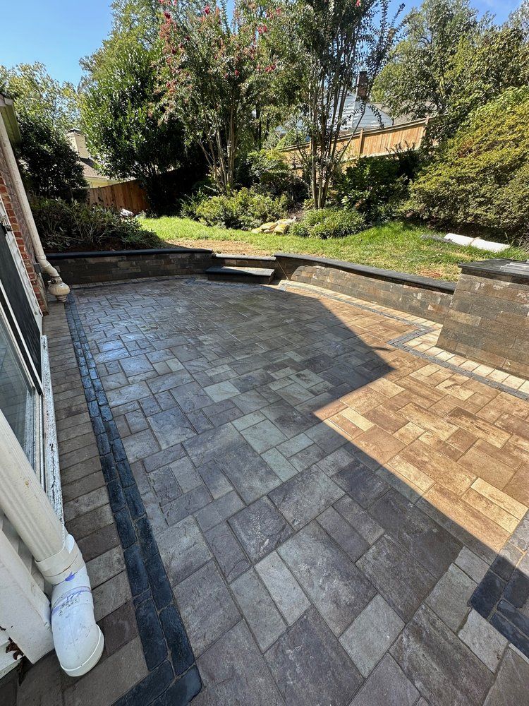 Brick patio with dark and light pavers. Steps lead to a grassy yard with trees.
