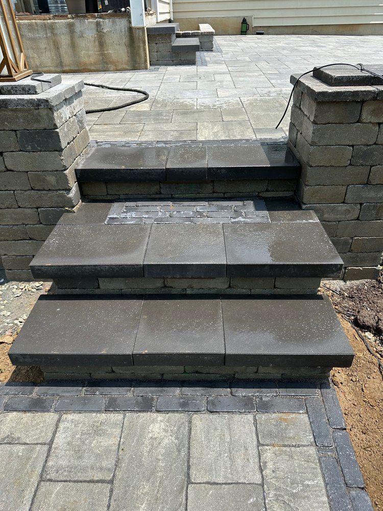 Stone steps leading up to a patio, with gray pavers and brick pillars.