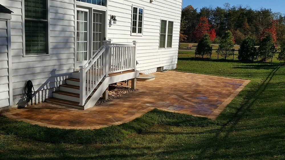Backyard patio with brown concrete, steps, and wooden railing leading to a white house.