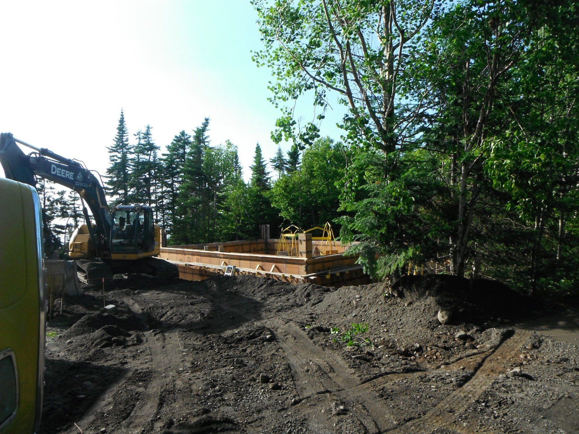 pelle mécanique à côté d'un coffrage de fondation en bordure de forêt