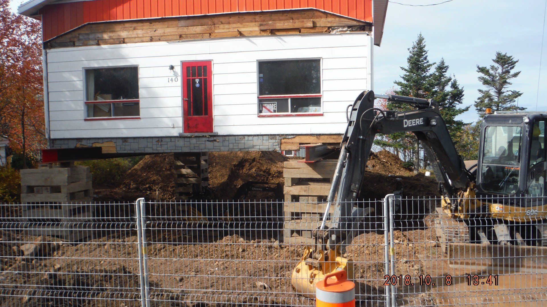 mini-excavatrice devant maison soulevée sur des piliers de bois