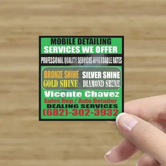 Hand holding a colorful business card advertising mobile detailing services with phone number.