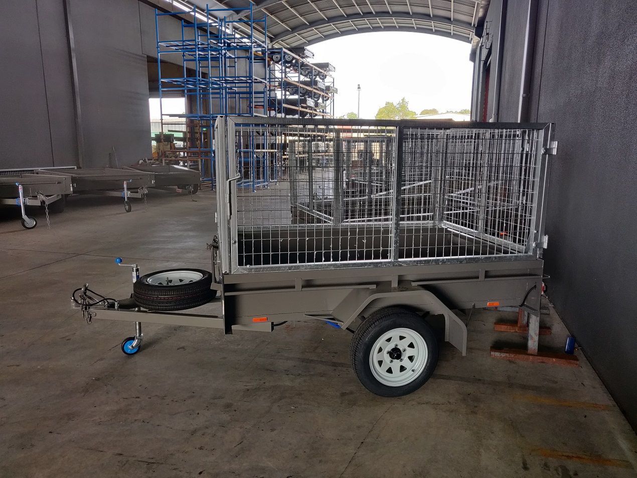 A single axel trailer with a cage on top is parked in a garage next to a building.