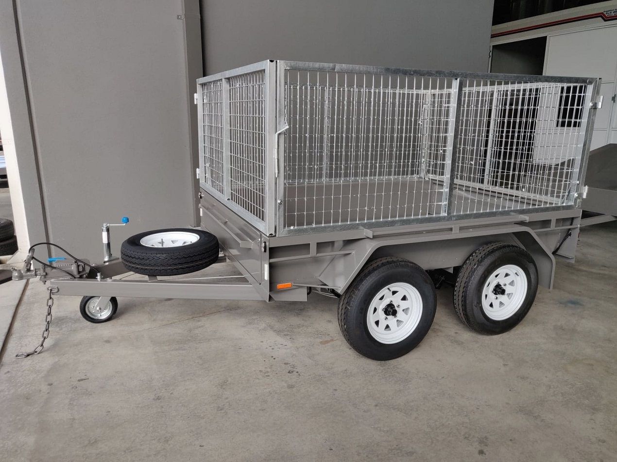 A tandem axel cage trailer with a spare wheel at the front is parked in a parking lot.