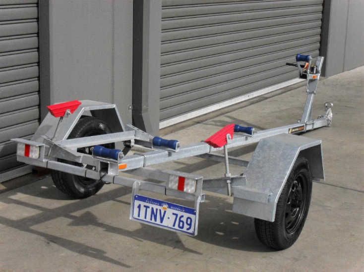 A single axel small boat trailer with a license plate is parked in front of a garage door.