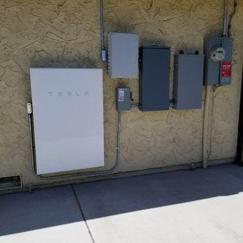 A tesla solar panel is mounted on the side of a building.