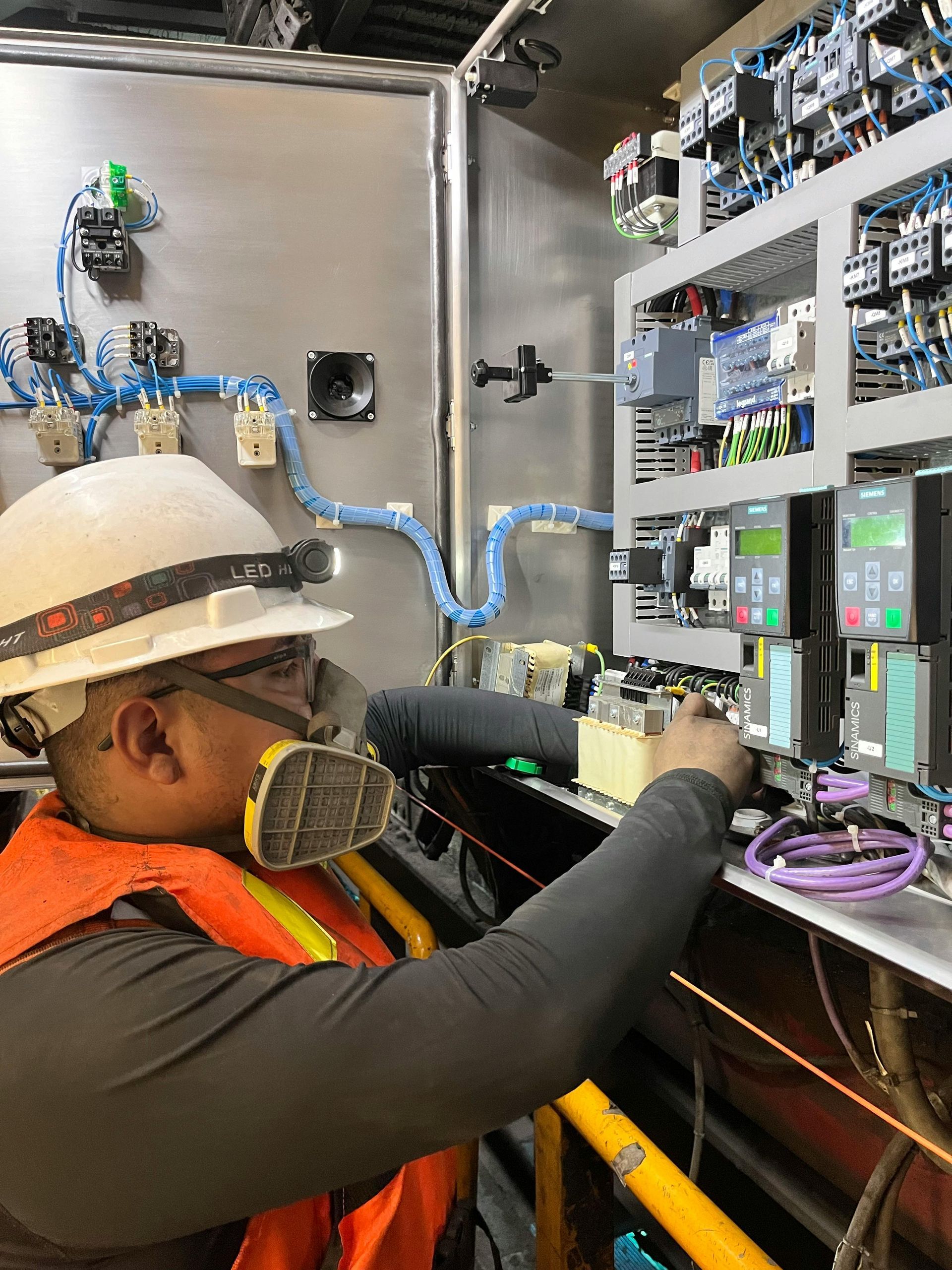 A man wearing a hard hat and safety vest is working on a machine.