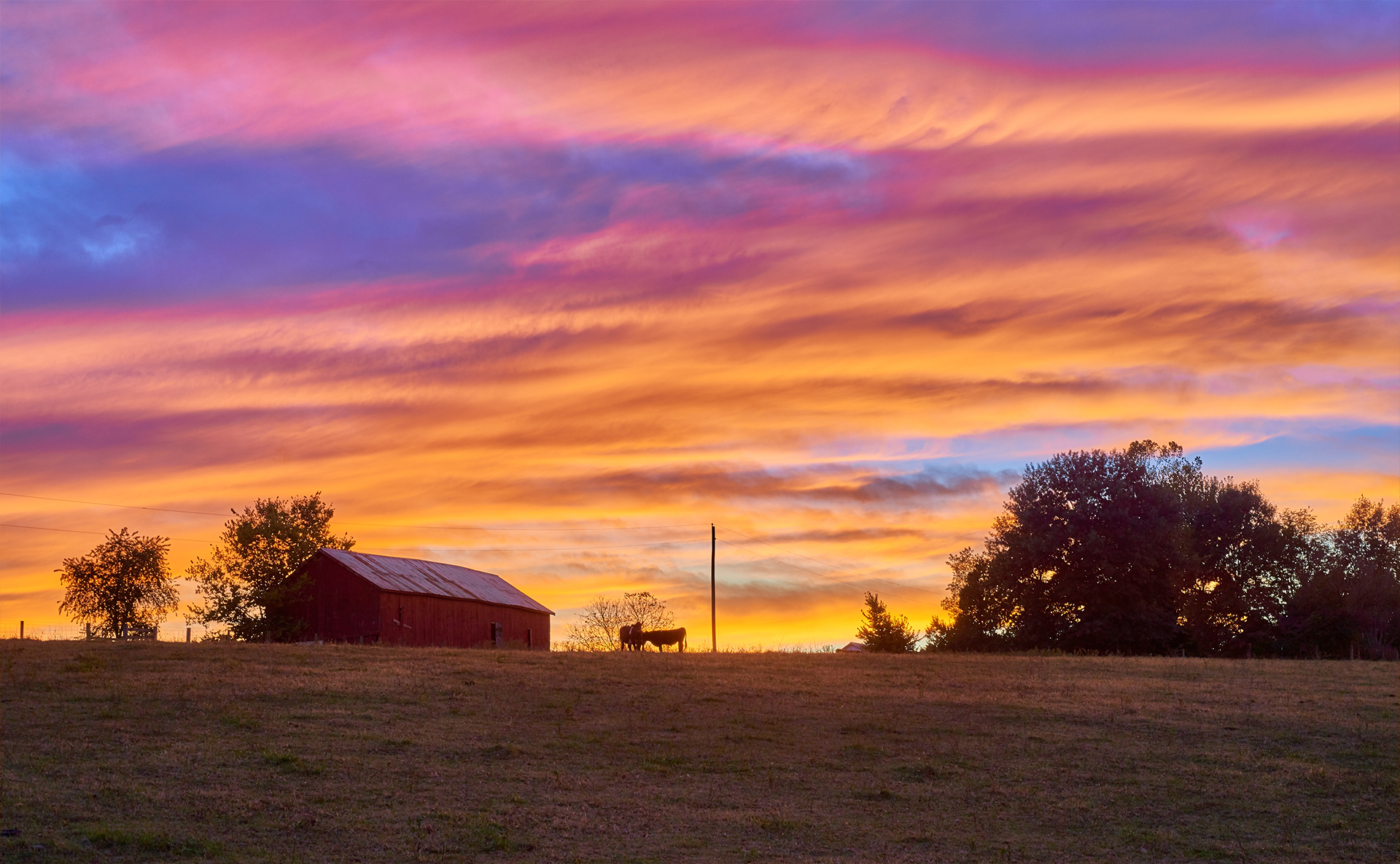 A barn is silhouetted against a colorful sunset sky.