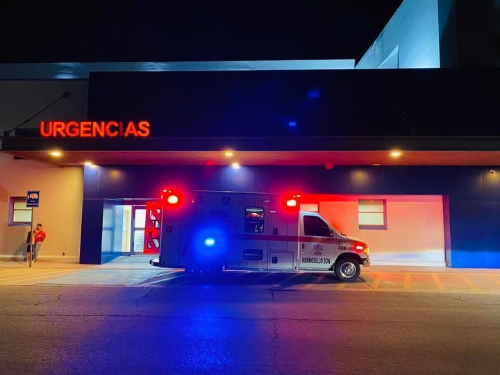 Una ambulancia está estacionada frente a una sala de emergencias por la noche.
