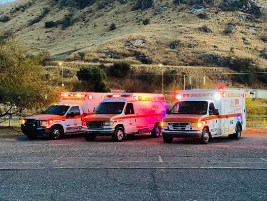 Tres camiones ambulancia están estacionados en un estacionamiento frente a una montaña.