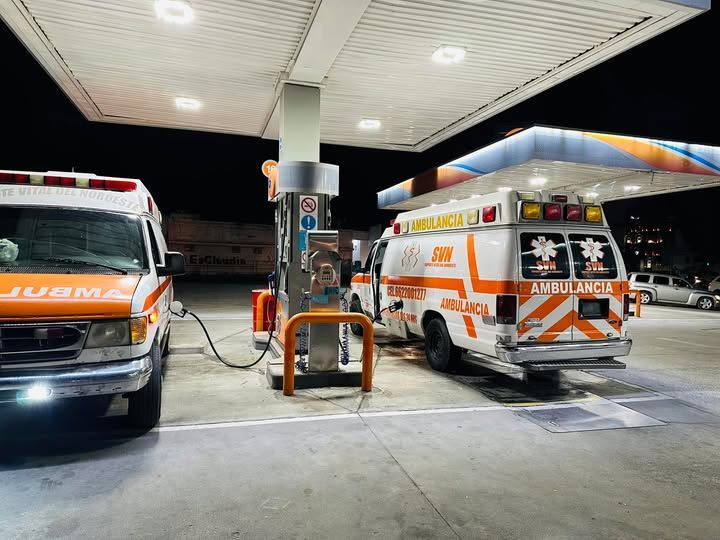 Dos ambulancias están estacionadas en una gasolinera por la noche.