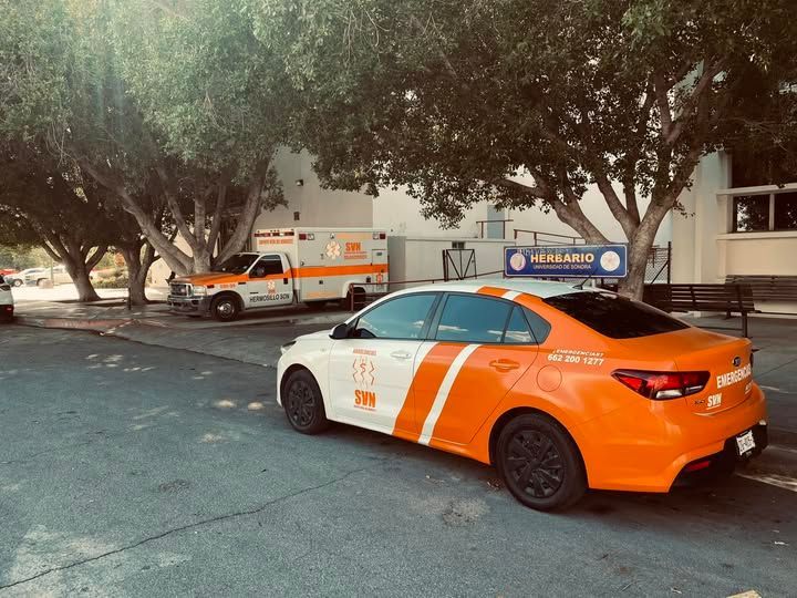Un coche naranja y blanco está aparcado junto a una ambulancia.