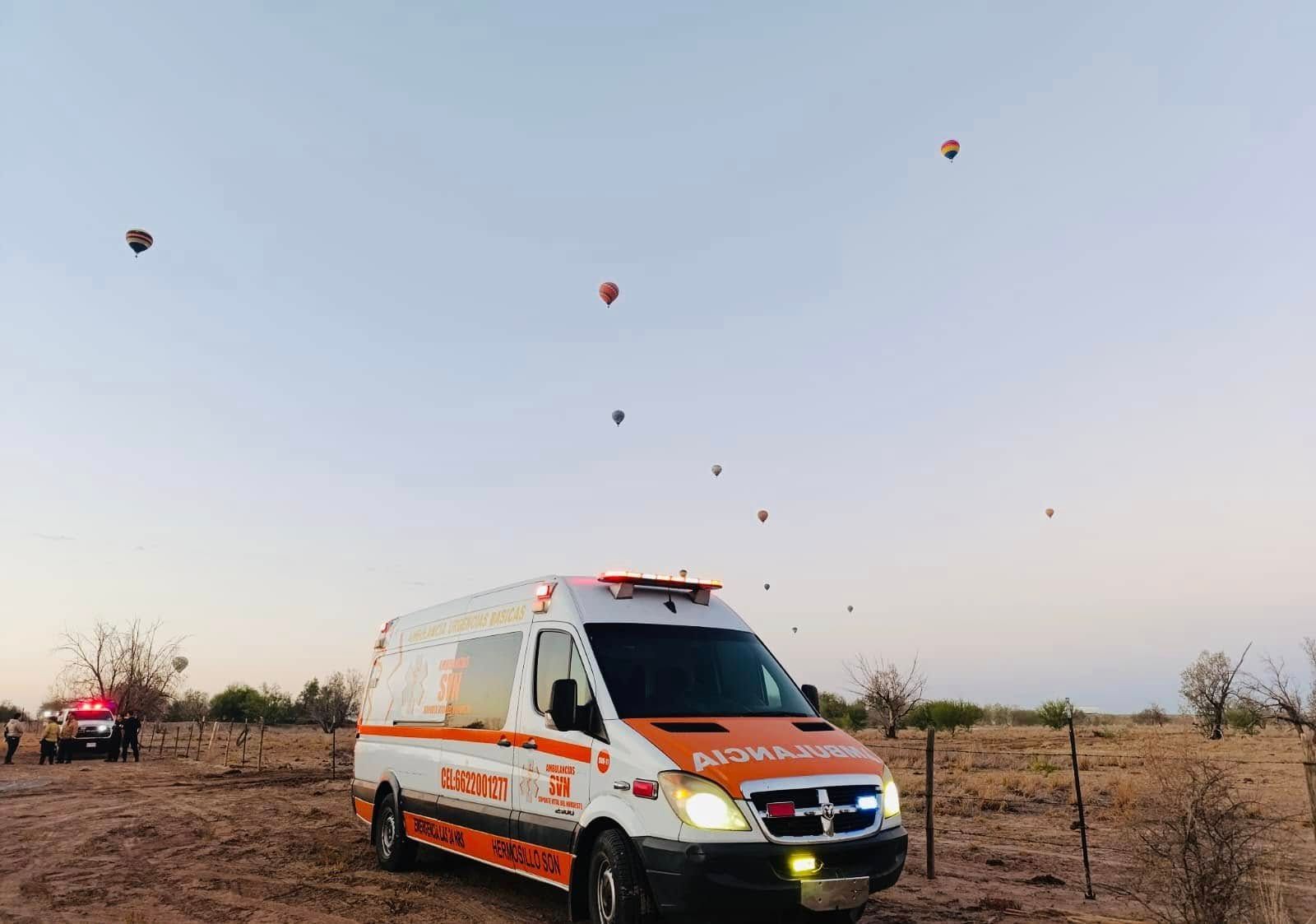 Una ambulancia está estacionada en un campo con globos aerostáticos al fondo.