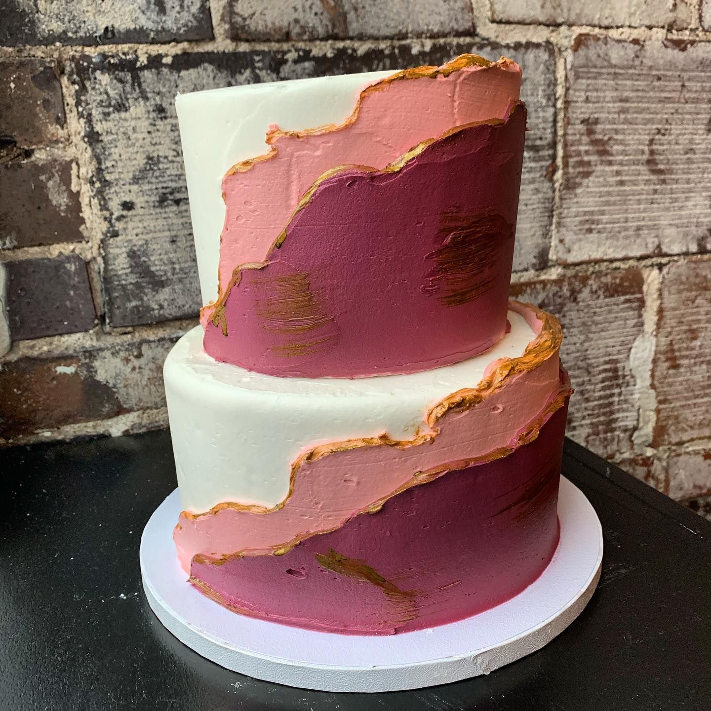 A pink and white cake sitting on a table in front of a brick wall.