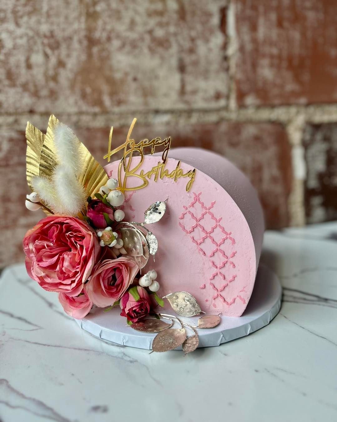 A pink birthday cake with flowers and feathers on a table.