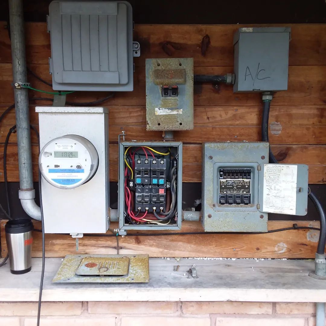 Electrical panel components mounted on wood siding, including a meter, breaker boxes, and conduit.