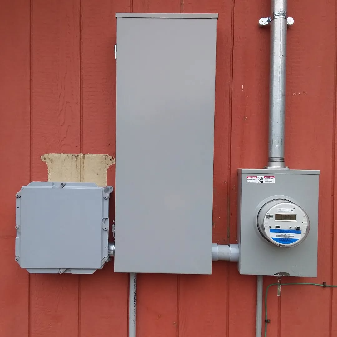 Electrical panel components on a red wooden wall: meter, box, conduit.