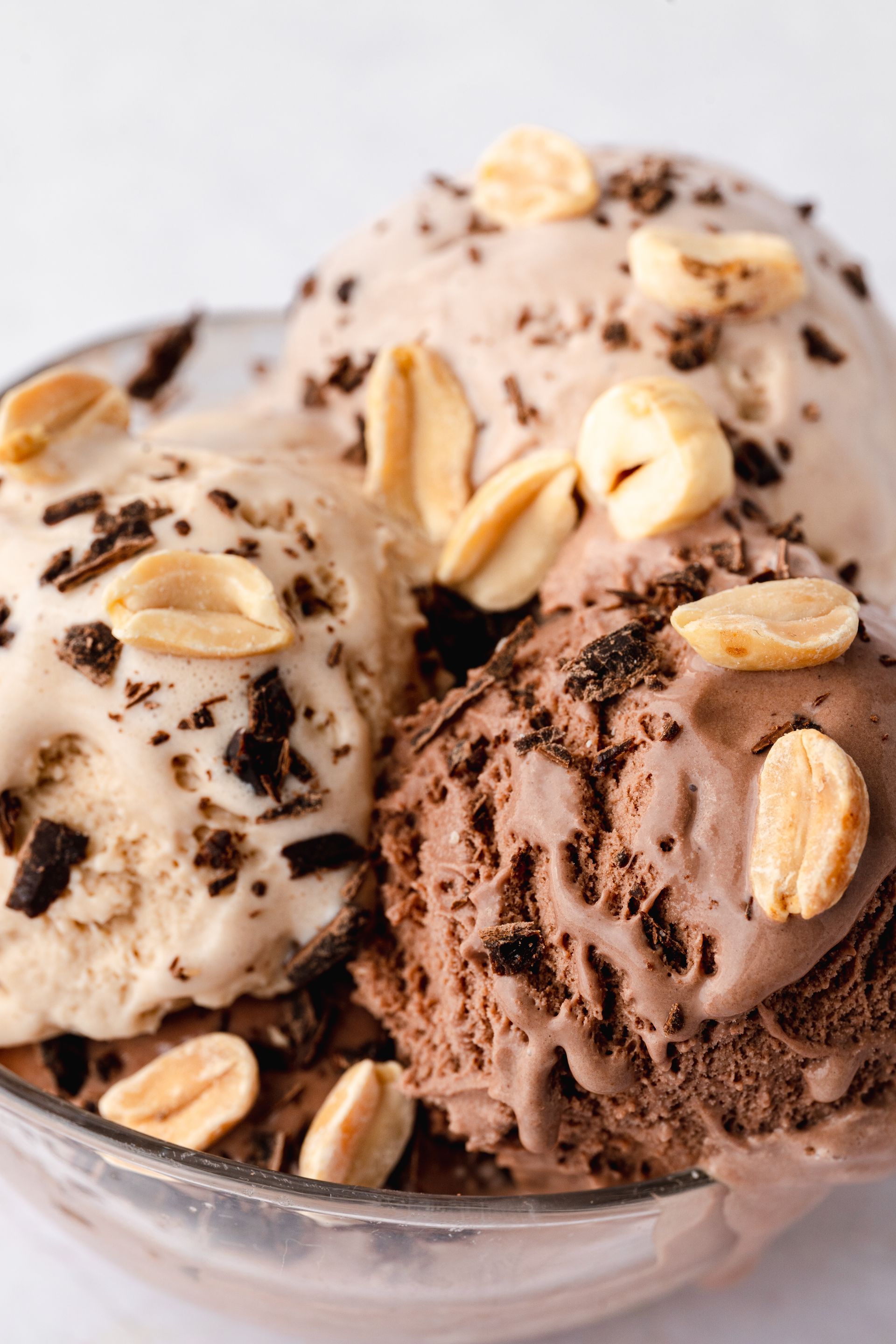 Skledica sladoleda z arašidi in čokoladnimi koščki na vrhu.